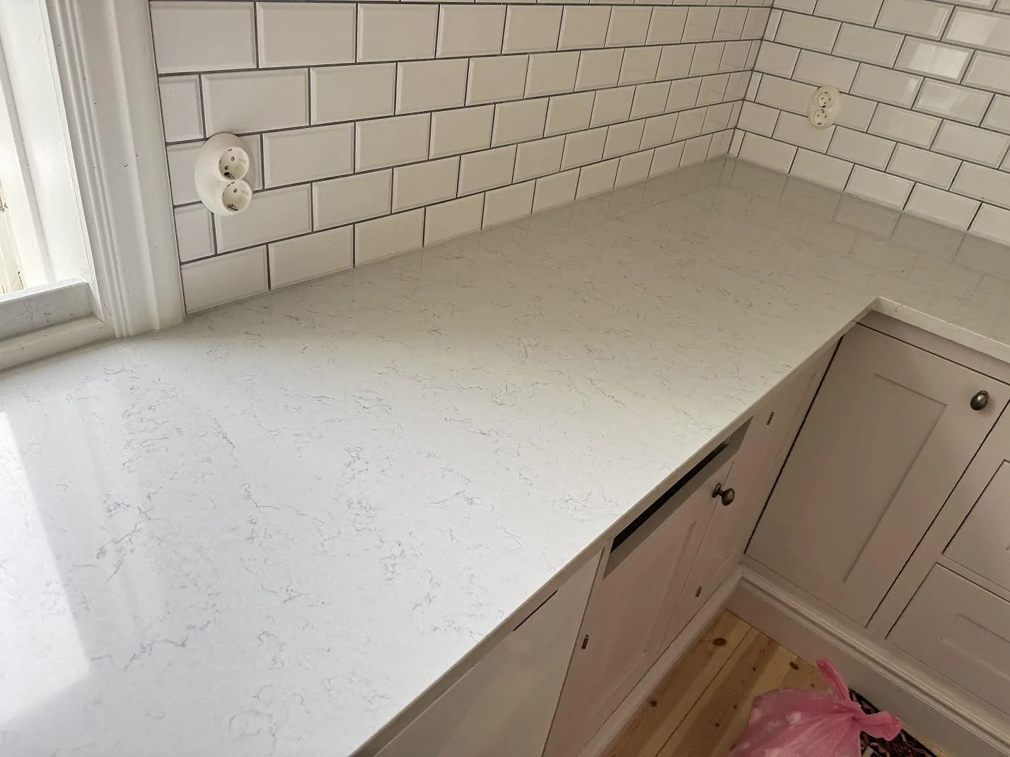 Köksbänkskiva i polerad Technistone Noble Carrara, ljus kvartskomposit, längs kaklad vägg i ett kök i Båstad.