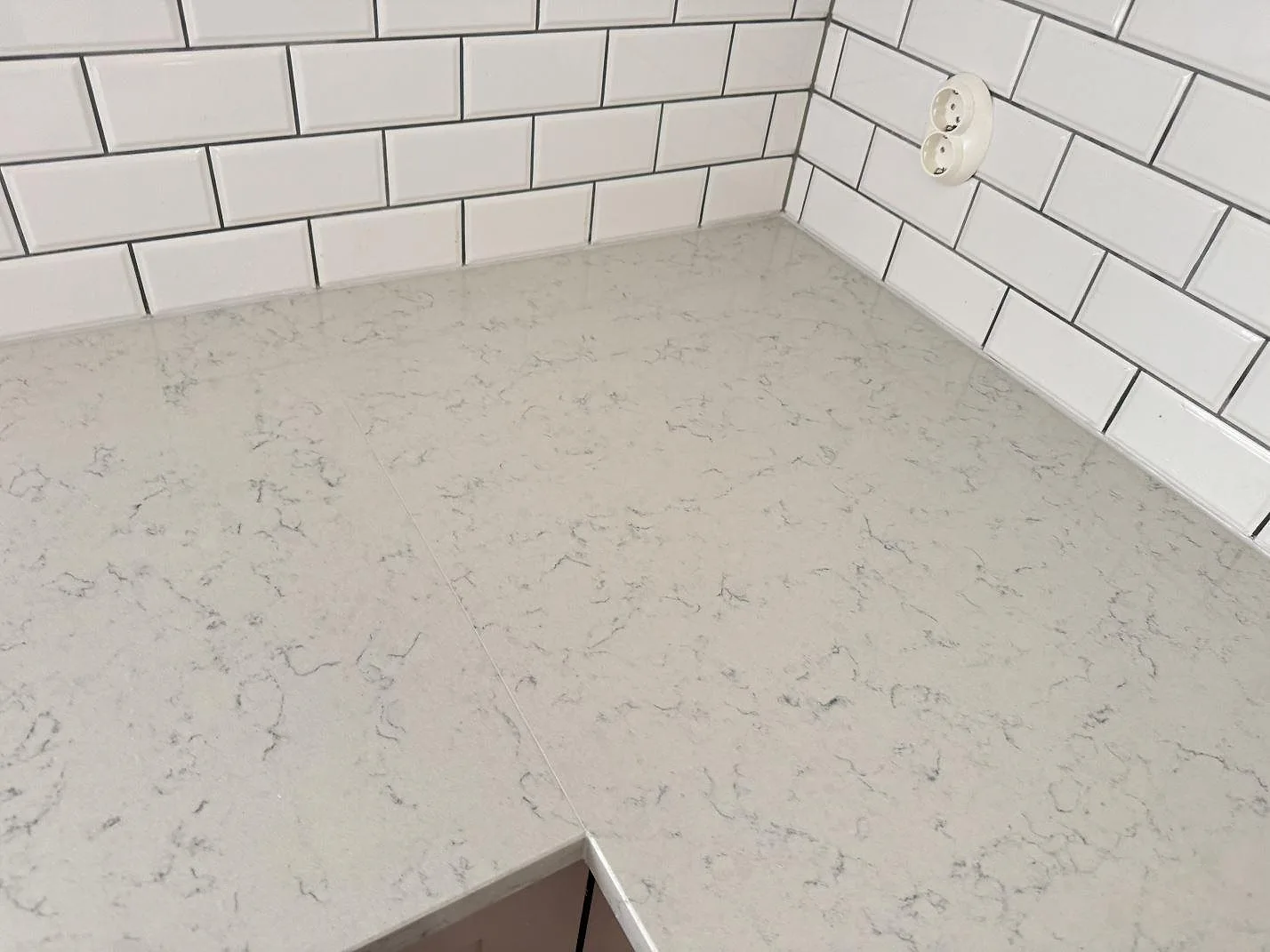 Detalj av hörnskarv i polerad Technistone Noble Carrara med grå ådring mot vit kakelvägg i Båstad.