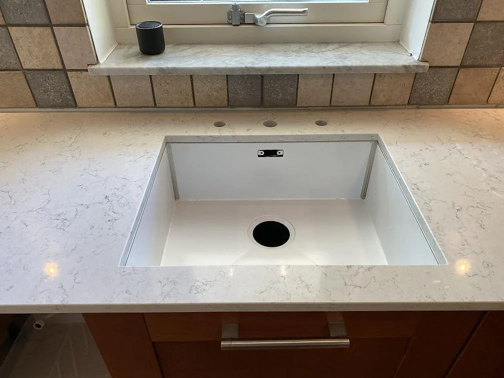 Vit diskho monterad under polerad Technistone Noble Carrara köksbänkskiva vid fönster i Blentarp.