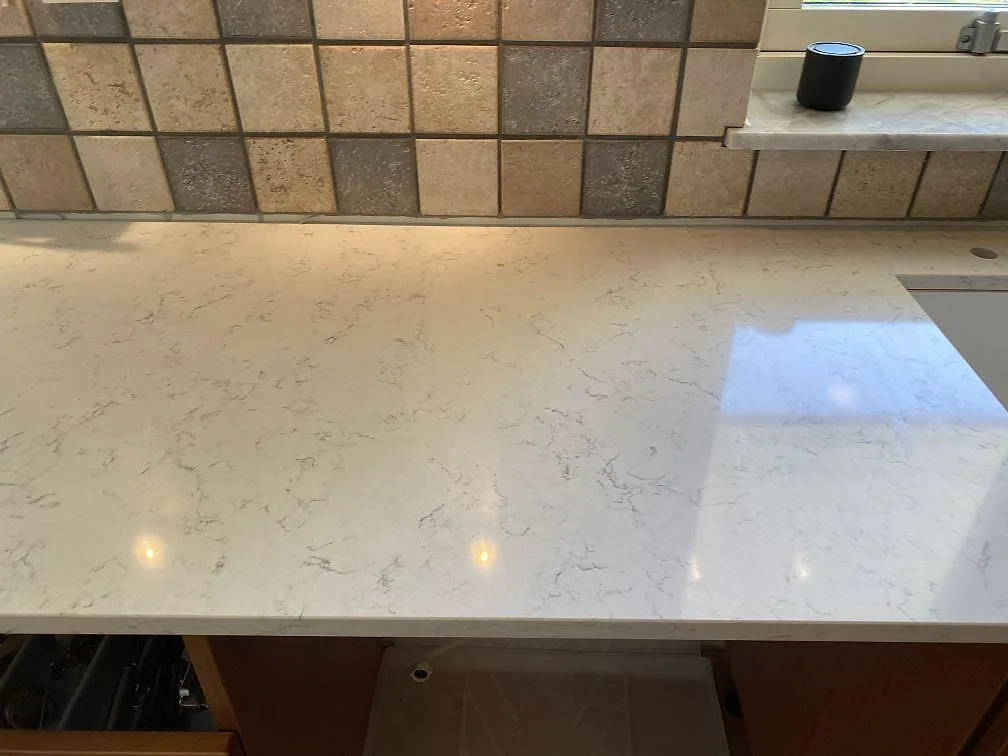 Polerad Technistone Noble Carrara bänkskiva med blank yta, ljus ådring och synlig diskhoöppning i Blentarp.