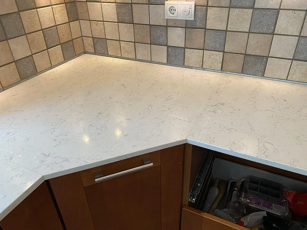 Hörnbänkskiva i polerad Technistone Noble Carrara kvartskomposit mot flerfärgat kakel i ett kök i Blentarp.