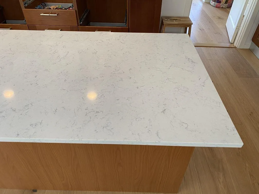 Polerad köksö i Technistone Noble Carrara kvartskomposit med ljus ådring och träfront i ett kök i Blentarp.