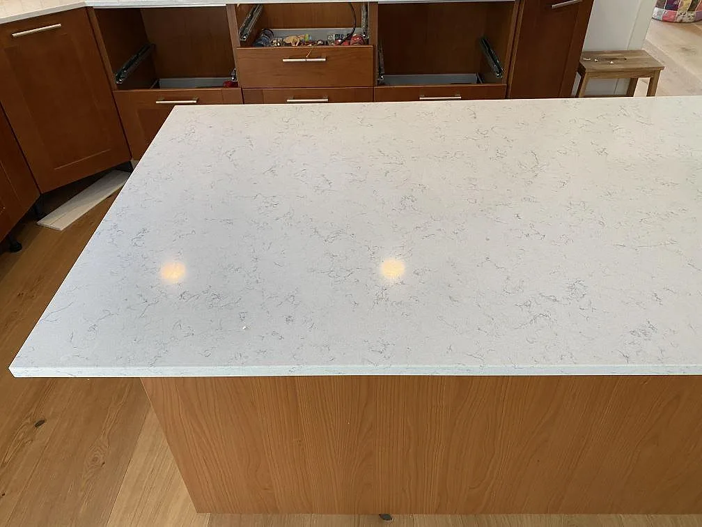 Närbild på polerad Technistone Noble Carrara köksö med ljus Carrara-ådring och träinredning i Blentarp.