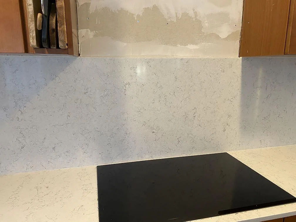 Polerad Technistone Noble Carrara vid hällen med matchande stänkskydd och träskåp i ett kök under montering i Blentarp.