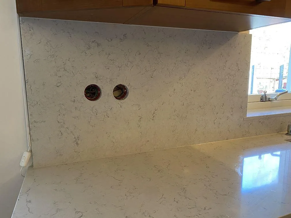 Blank bänkskiva och stänkskydd i Technistone Noble Carrara vid diskbänk och väggskåp i ett kök i Blentarp.