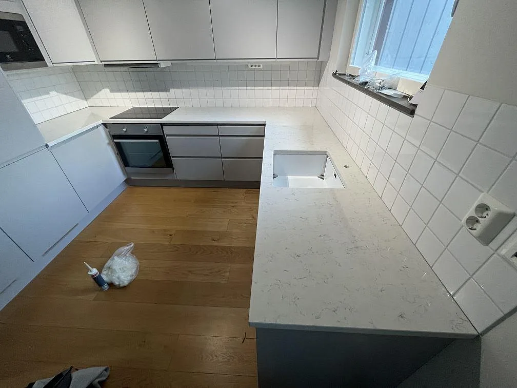 Köksbänkskiva i vit Technistone Noble Carrara, polerad kvartskomposit, med häll och urtag för diskho i ett U-format kök i Bromma.