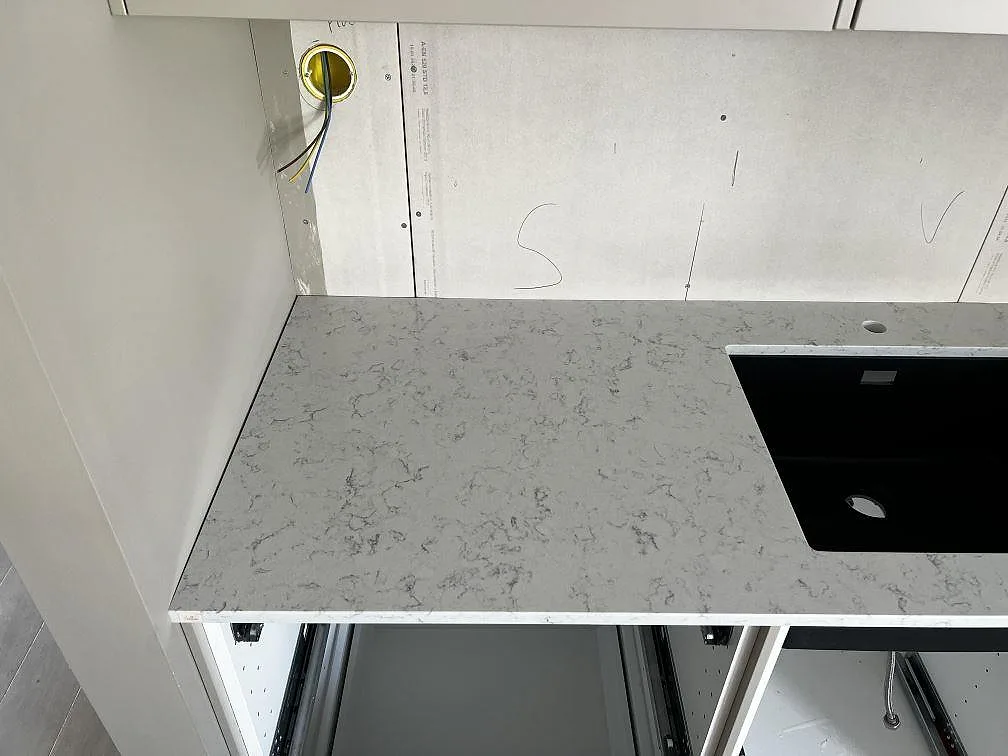Närbild på polerad Technistone Noble Carrara, vit komposit med grå ådring, intill den svarta diskhon i Fjälkinge.