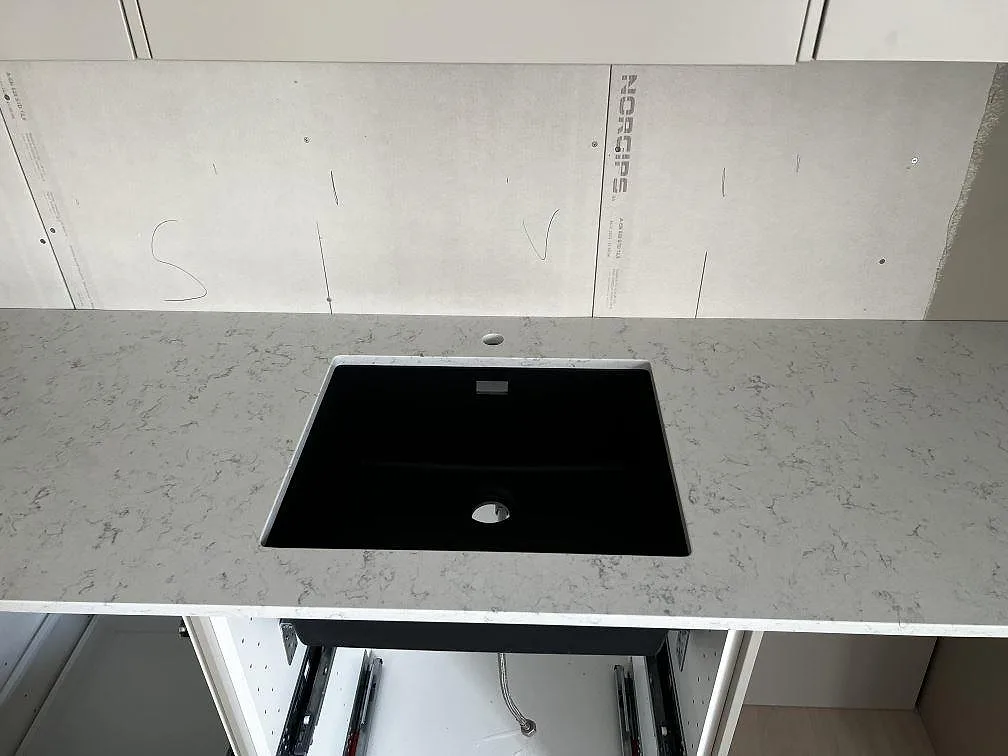 Svart underlimmad diskho i en 20 mm polerad köksbänkskiva av Technistone Noble Carrara i ett kök i Fjälkinge.