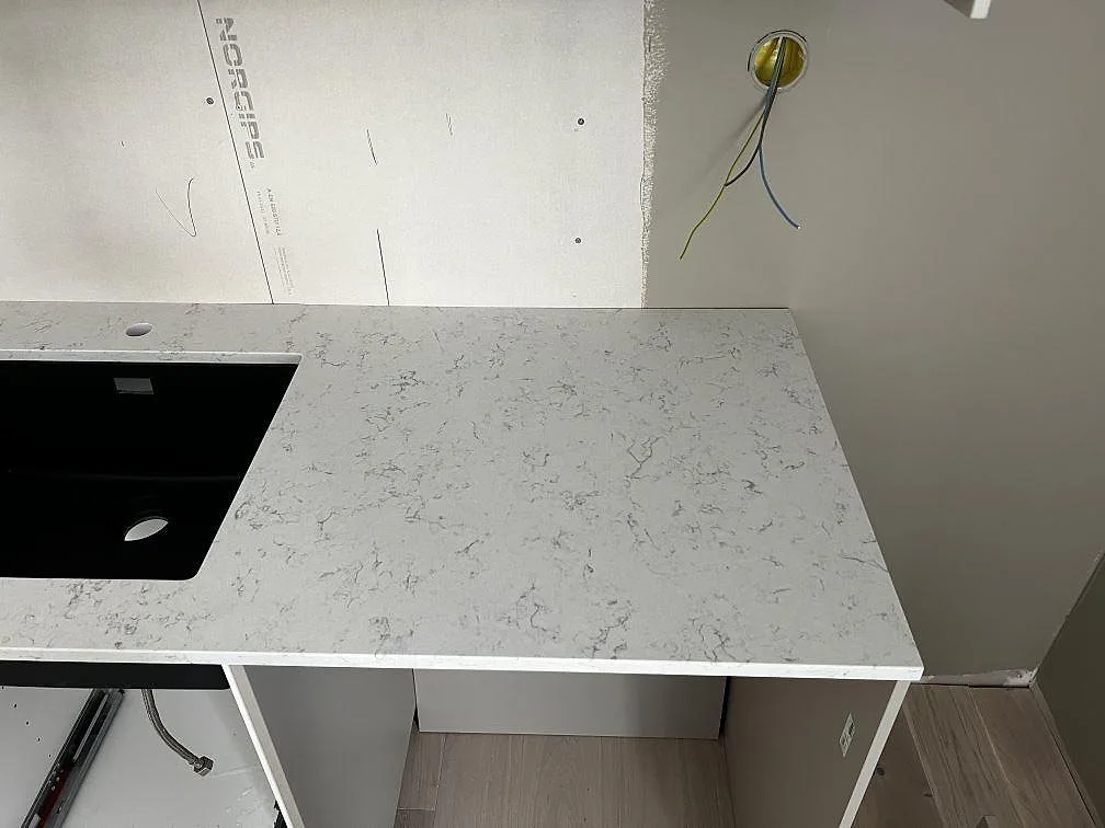 Höger sida av köksbänk i polerad Technistone Noble Carrara med svart diskho och ljusgrå ådring i Fjälkinge.