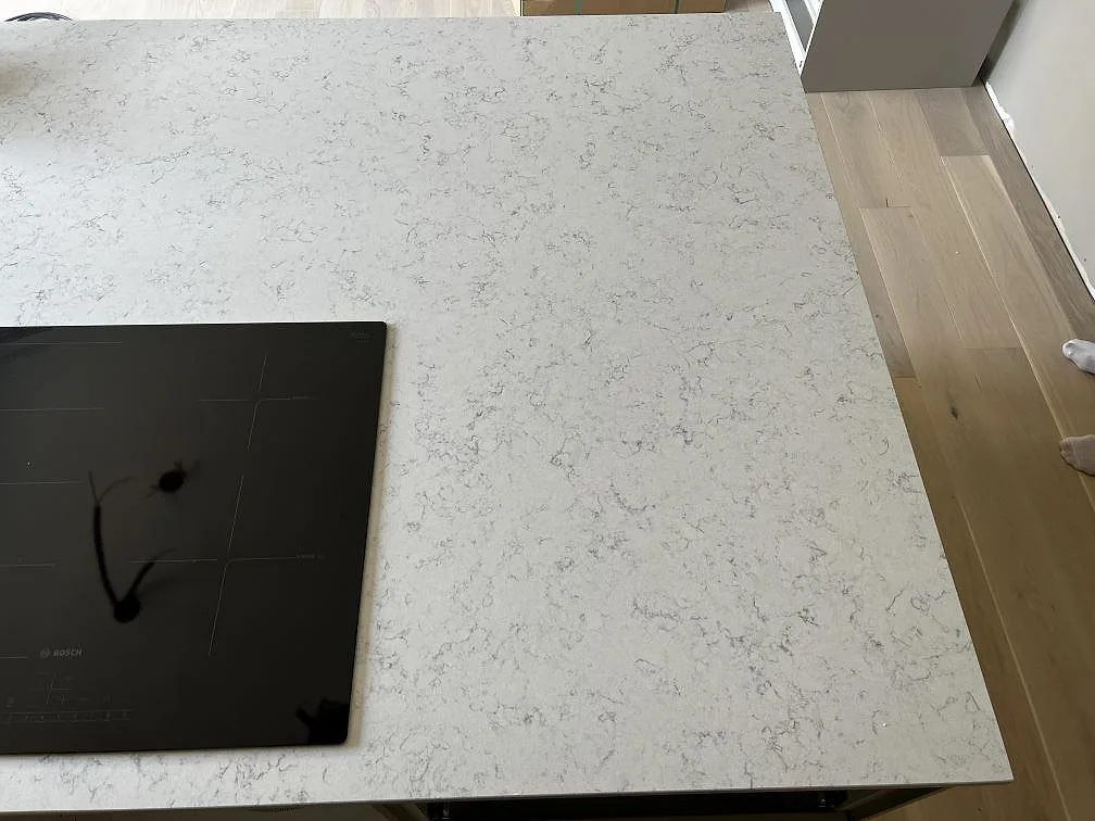 Köksö i polerad Technistone Noble Carrara med svart induktionshäll och grå ådring sedd ovanifrån i Fjälkinge.