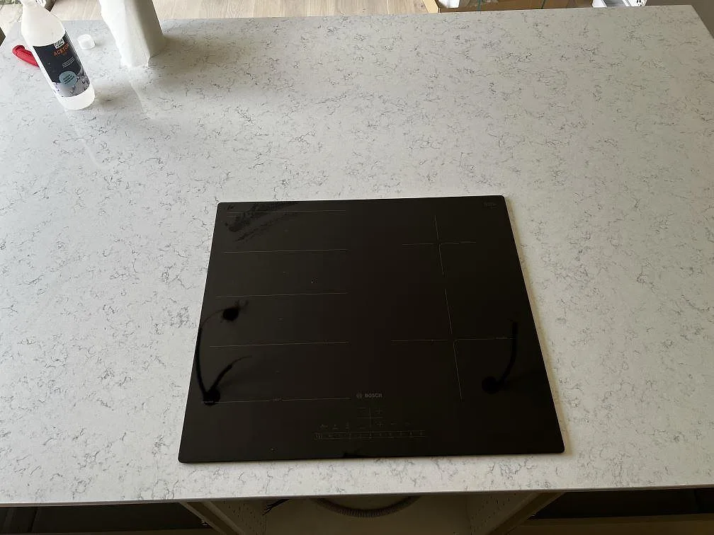 Svart induktionshäll monterad i en polerad kompositbänkskiva av Technistone Noble Carrara i Fjälkinge.