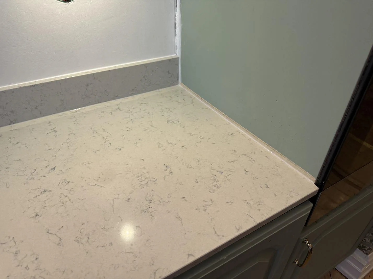 Detaljbild av vitgrå Technistone Noble Carrara bänkskiva, polerad, intill gröngrå köksinredning i Göteborg.