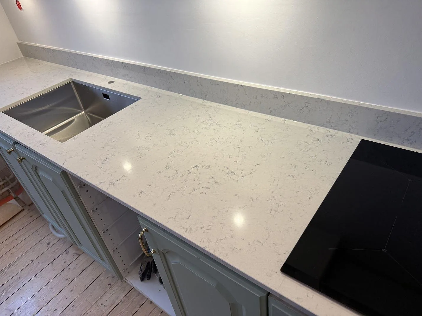 Köksbänkskiva i vit Technistone Noble Carrara komposit, polerad, med rostfri diskho, svart induktionshäll och låg stänkkant i Göteborg.
