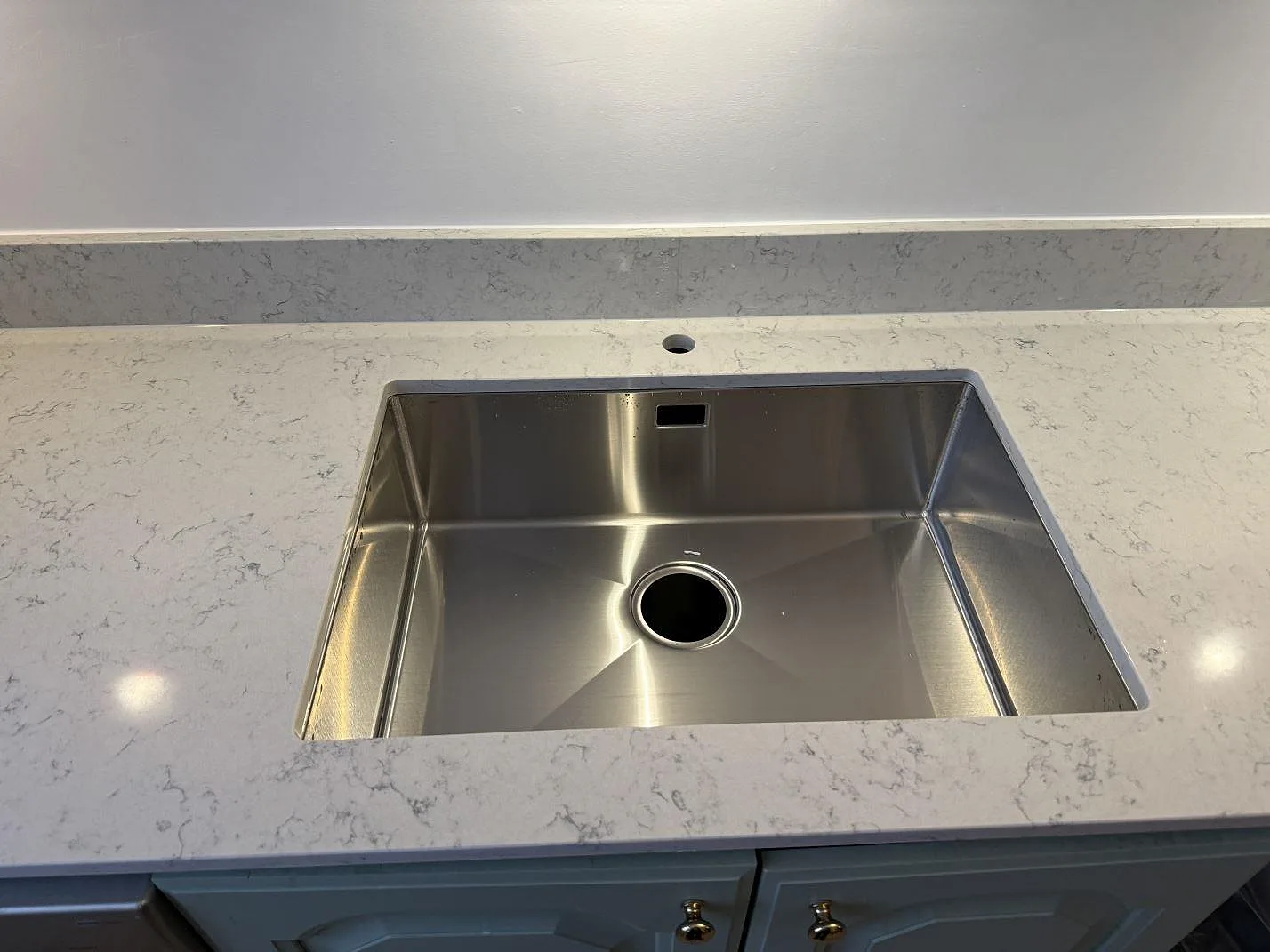 Rostfri diskho monterad i vit Technistone Noble Carrara komposit med låg stänkkant bakom bänkskivan i Göteborg.