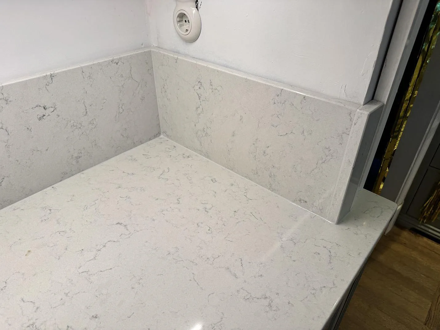 Detalj av polerad Technistone Noble Carrara som badrumsbänkskiva med uppvikta stenskivor och sidostycke i Göteborg.