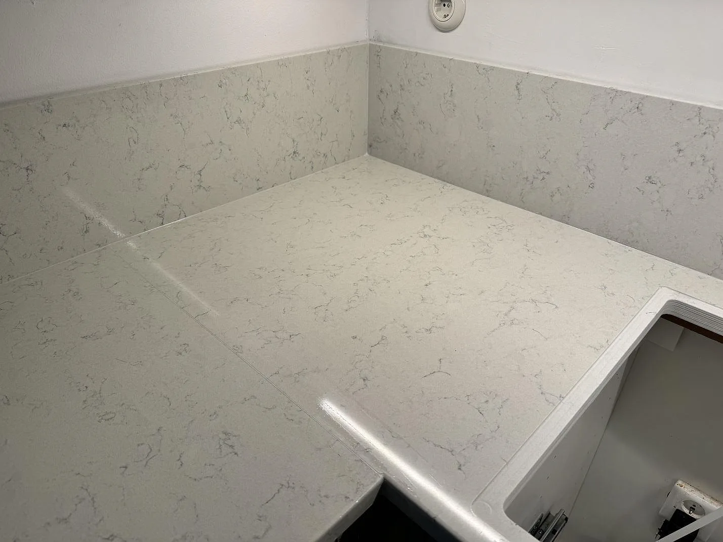 Polerad bänkskiva i Technistone Noble Carrara med grå ådring, stänkskydd och öppning för tvättställ i ett badrum i Göteborg.