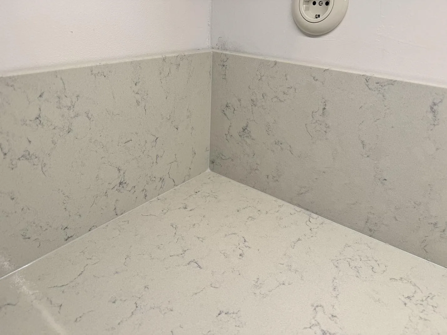 Närbild på hörn med bänkskiva och väggskivor i polerad Technistone Noble Carrara komposit i Göteborg.