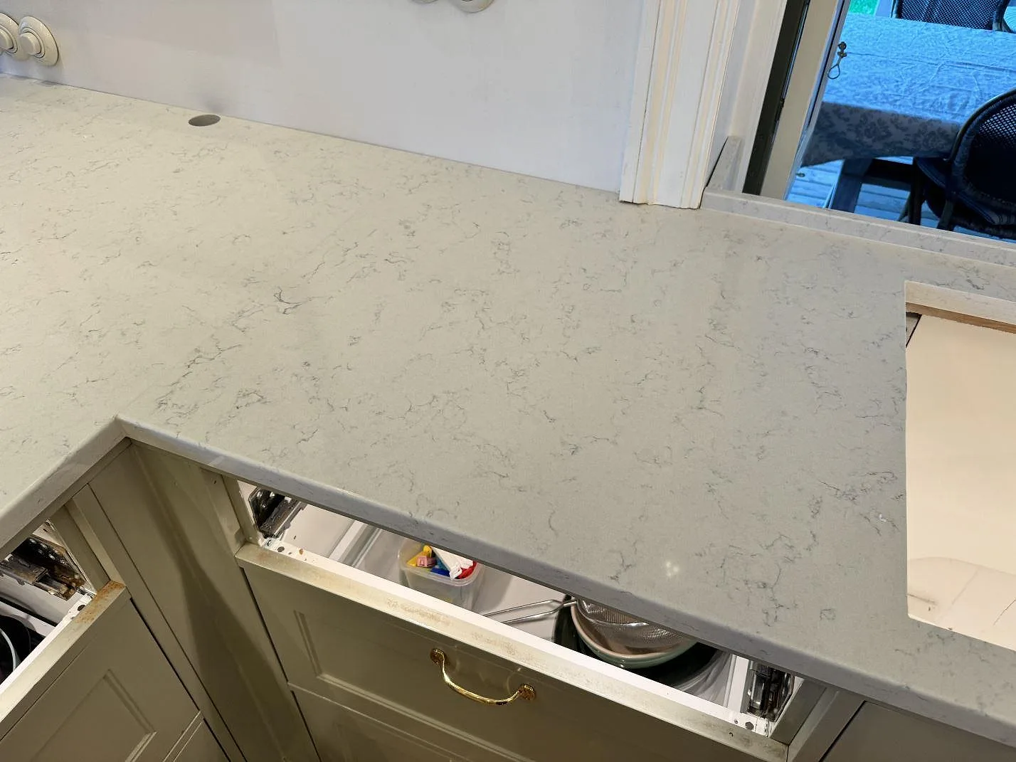 Lång bänkyta i polerad Technistone Noble Carrara med tvättställsöppning, gröna luckor och ljus kompositsten i Göteborg.
