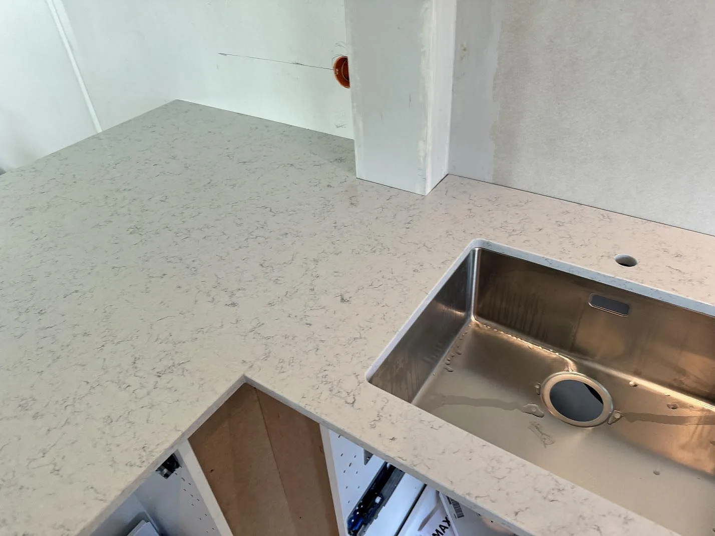 Närbild av polerad Technistone Noble Carrara köksbänkskiva i vit kvartskomposit med rostfri diskho och hörnpassning i Göteborg.