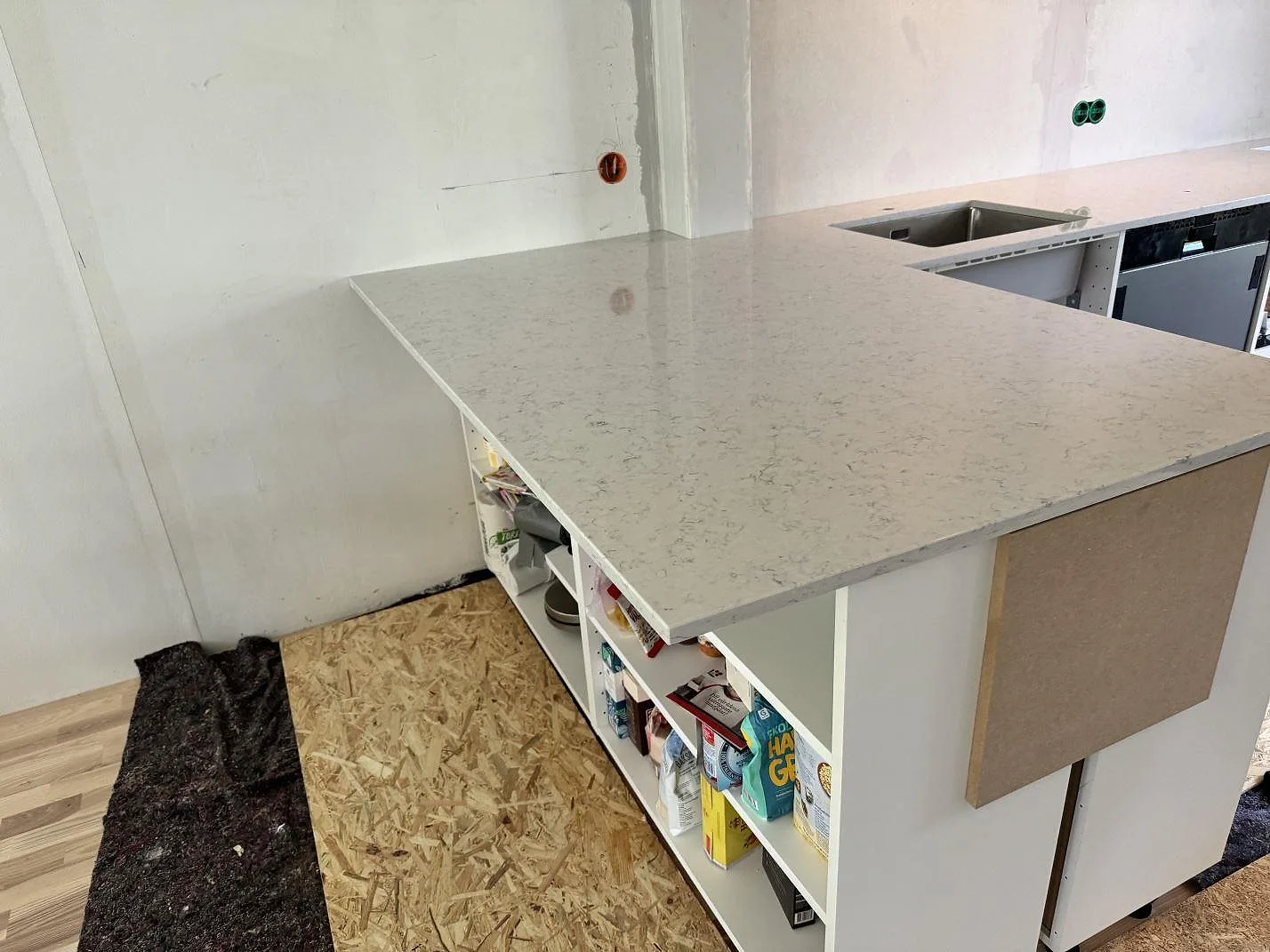 Större arbetsyta i polerad Technistone Noble Carrara, ljus kvartskomposit, med diskho i bakre bänk under montering i Göteborg.