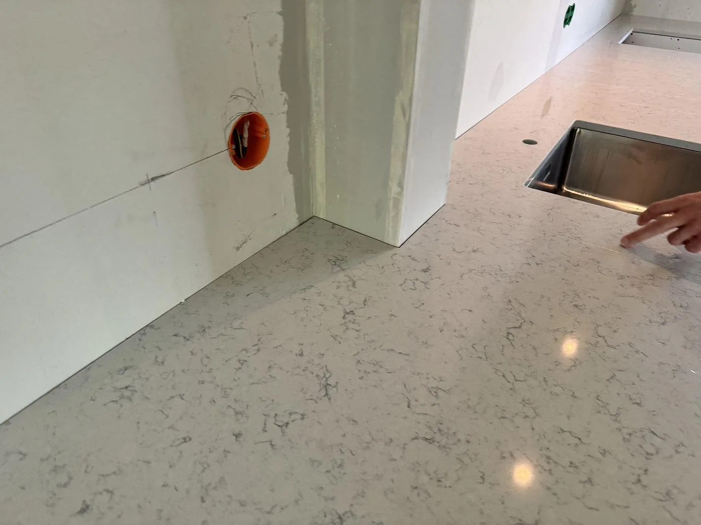 Detalj av polerad Technistone Noble Carrara köksbänkskiva med grå ådring, diskho i bakgrunden och monteringsmarkeringar i Göteborg.
