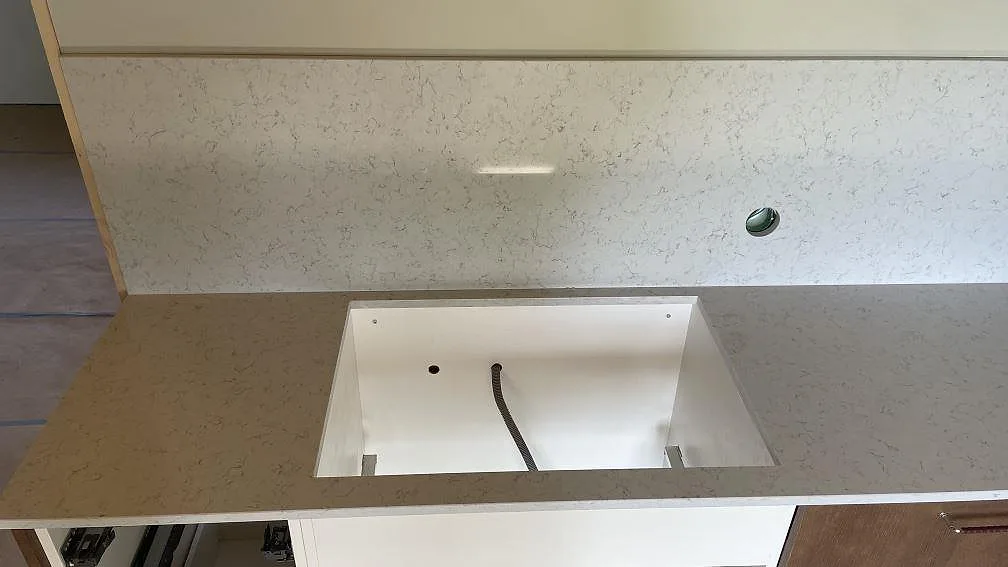 Köksbänk i polerad Technistone Noble Carrara komposit med stor utskärning och matchande stänkskydd i Hagby.