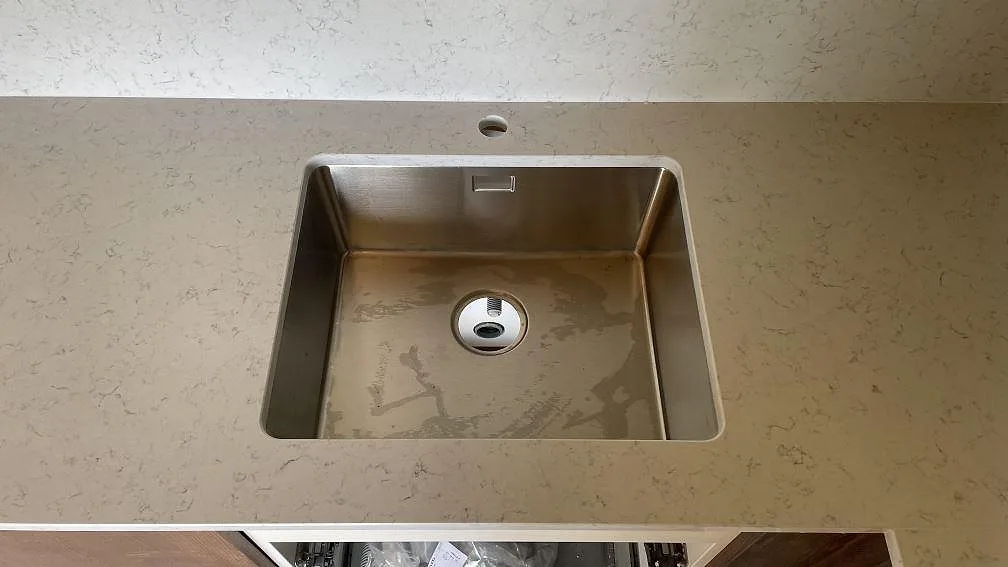 Närbild på rostfri diskho i polerad Technistone Noble Carrara komposit med ljus grå ådring i kök i Hagby.