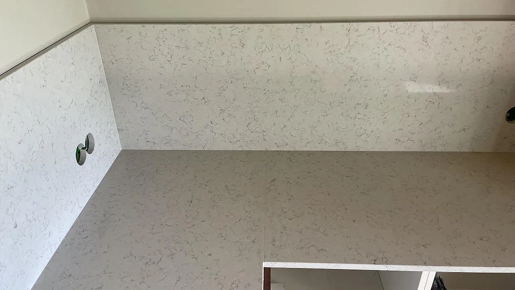 Hörnparti med bänkskiva och stänkskydd i polerad Technistone Noble Carrara komposit i ett kök i Hagby.