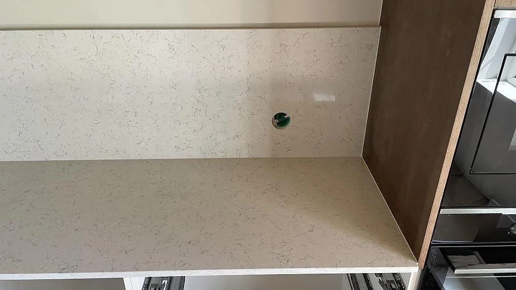 Rak köksbänk i polerad Technistone Noble Carrara komposit med ljus ådring, stänkskydd och inbyggda ugnar i Hagby.