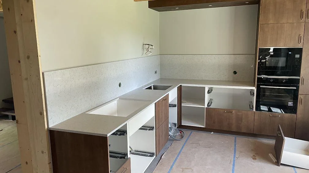 Köksbänkskiva i vit Technistone Noble Carrara komposit, polerad, med matchande stänkskydd i ett kök under montering i Hagby.