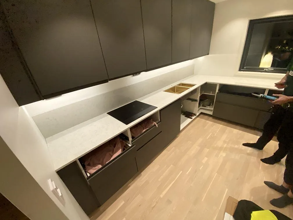 Köksbänkskiva i vit Technistone Noble Carrara, polerad kvartskomposit, under montering i ett kök i Halmstad med induktionshäll och underlimmad diskho.