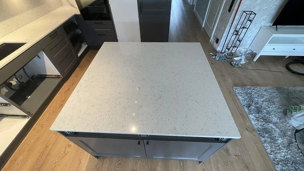 Polerad köksö i Technistone Noble Carrara komposit med ljus botten och grå ådring i ett kök under montering i Jönköping.