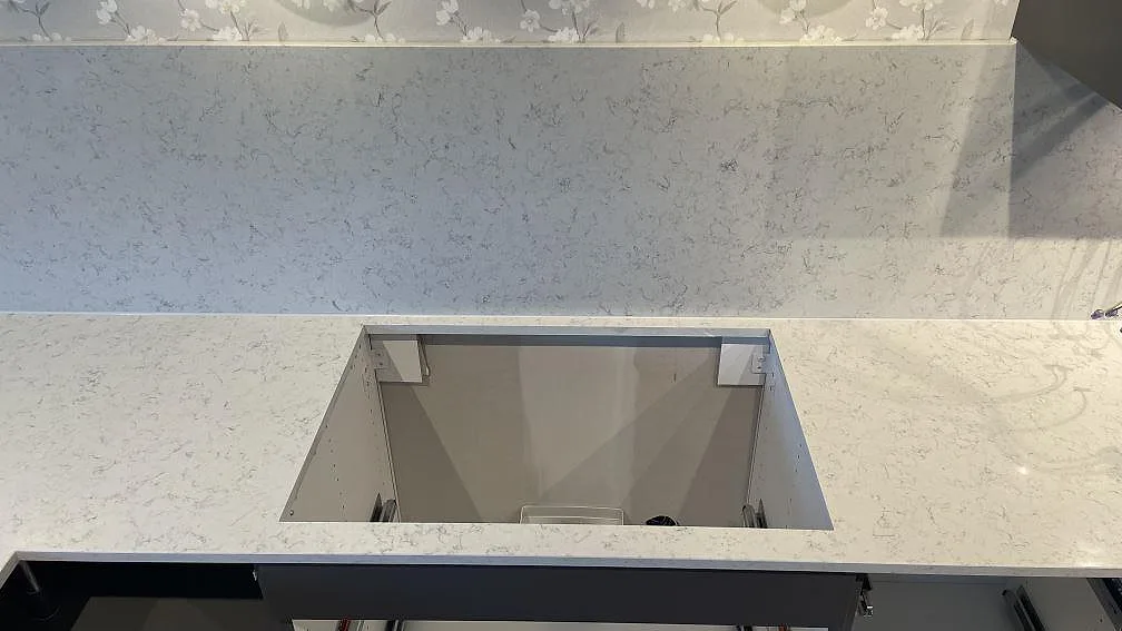 Närbild av köksbänkskivan i Technistone Noble Carrara med uppvikt stänkskydd och rektangulär utskärning i ett kök i Jönköping.