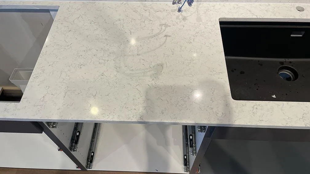 Detalj av Technistone Noble Carrara bänkskiva, polerad komposit, med svart diskho, utskärning och blandarhål i köket i Jönköping.