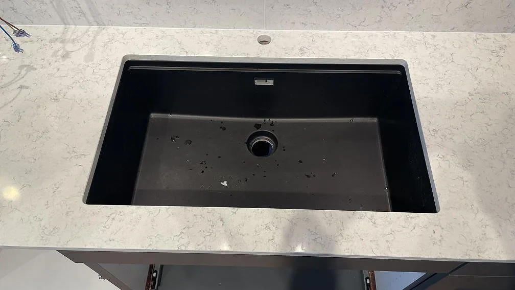 Svart diskho monterad i en polerad bänkskiva av Technistone Noble Carrara komposit med ljus ådring i Jönköping.