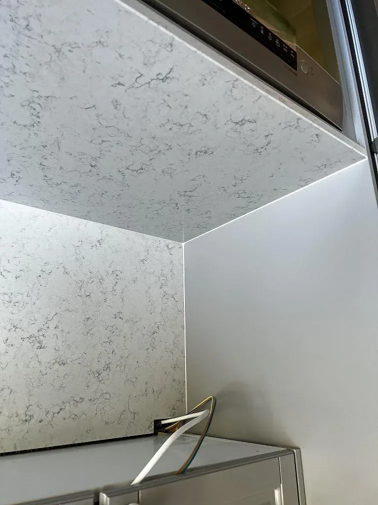 Närbild på den polerade ytan och stänkkanten i vit Technistone Noble Carrara med grå ådring i ett kök i Klippan.