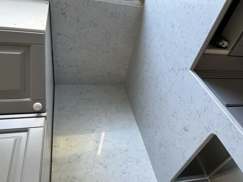 Underlimmad rostfri diskho i bänkskiva av vit Technistone Noble Carrara med uppvikt stänkkant i ett kök i Klippan.