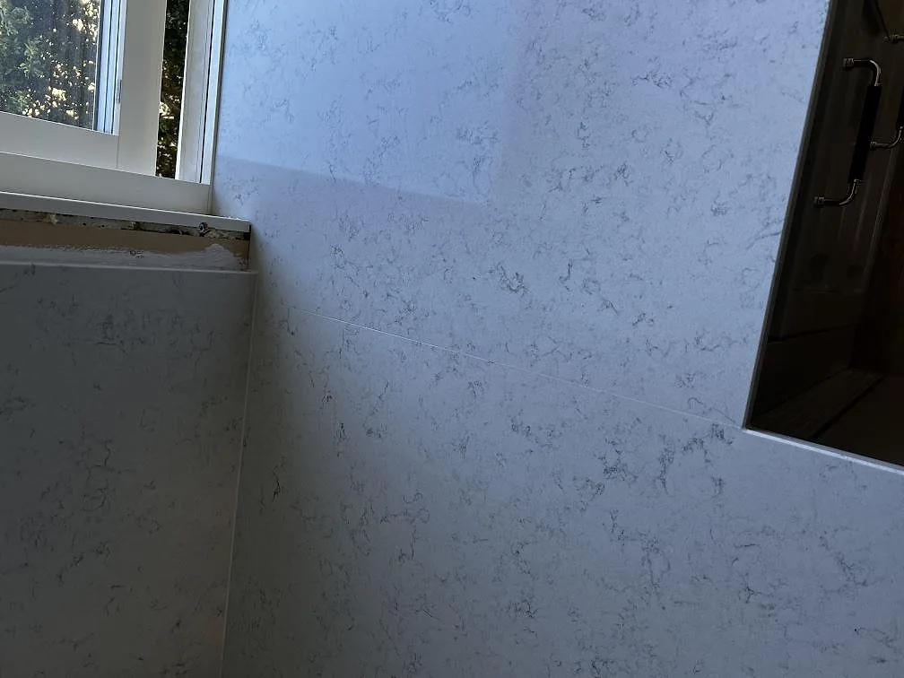 Hörn av köksbänkskiva i Technistone Noble Carrara i Klippan med två underlimmade rostfria diskhoar och polerad yta.