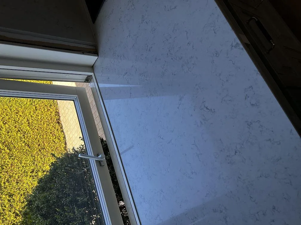 Stänkkant och bänkskiva i vit Technistone Noble Carrara vid fönster i ett kök i Klippan, polerad kvartskomposit.