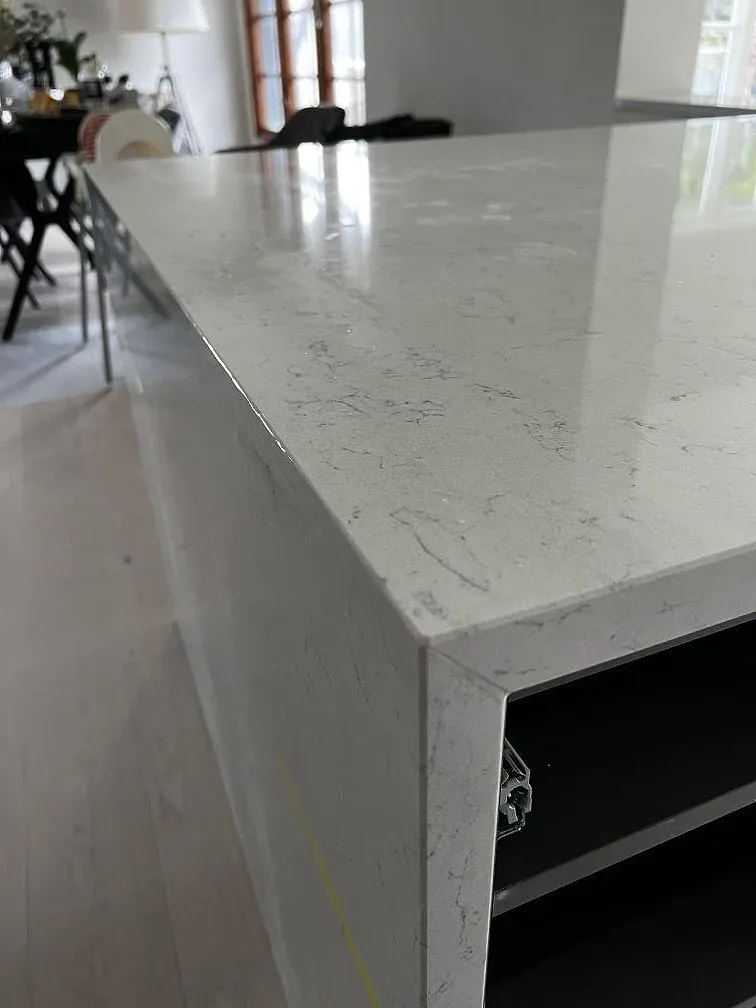 Närbild på köksön i vit Technistone Noble Carrara med mjuk grå ådring och polerad kant i ett kök i Kristianstad.