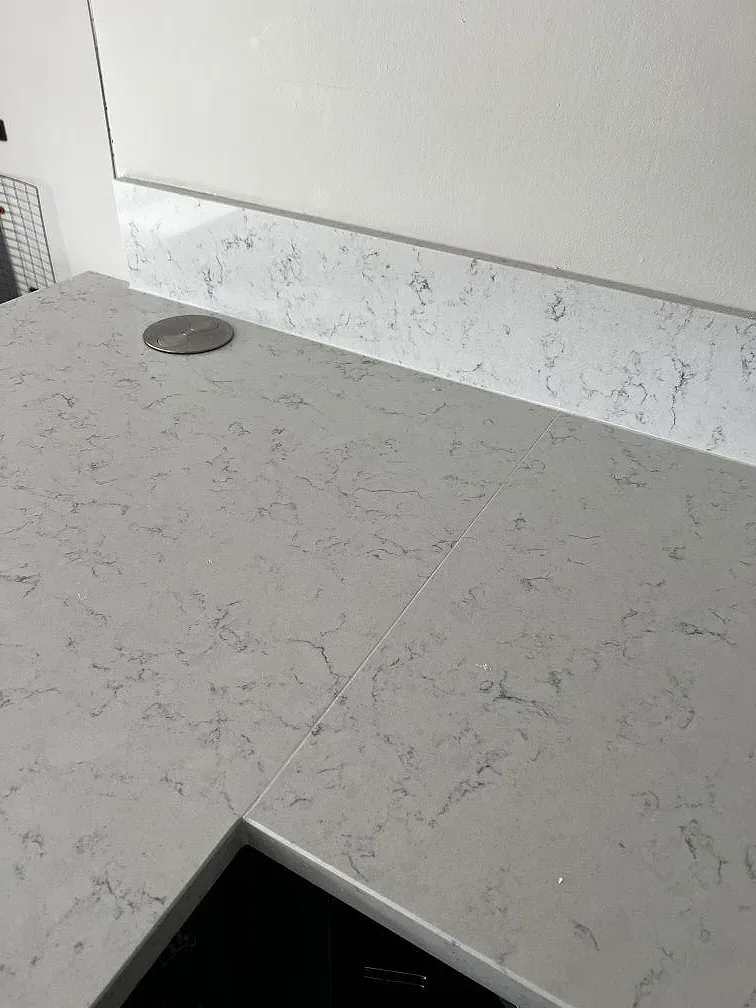 Bänkskiva i vit Technistone Noble Carrara sedd ovanifrån med synlig skarv och popup-uttag i ett kök i Kristianstad.