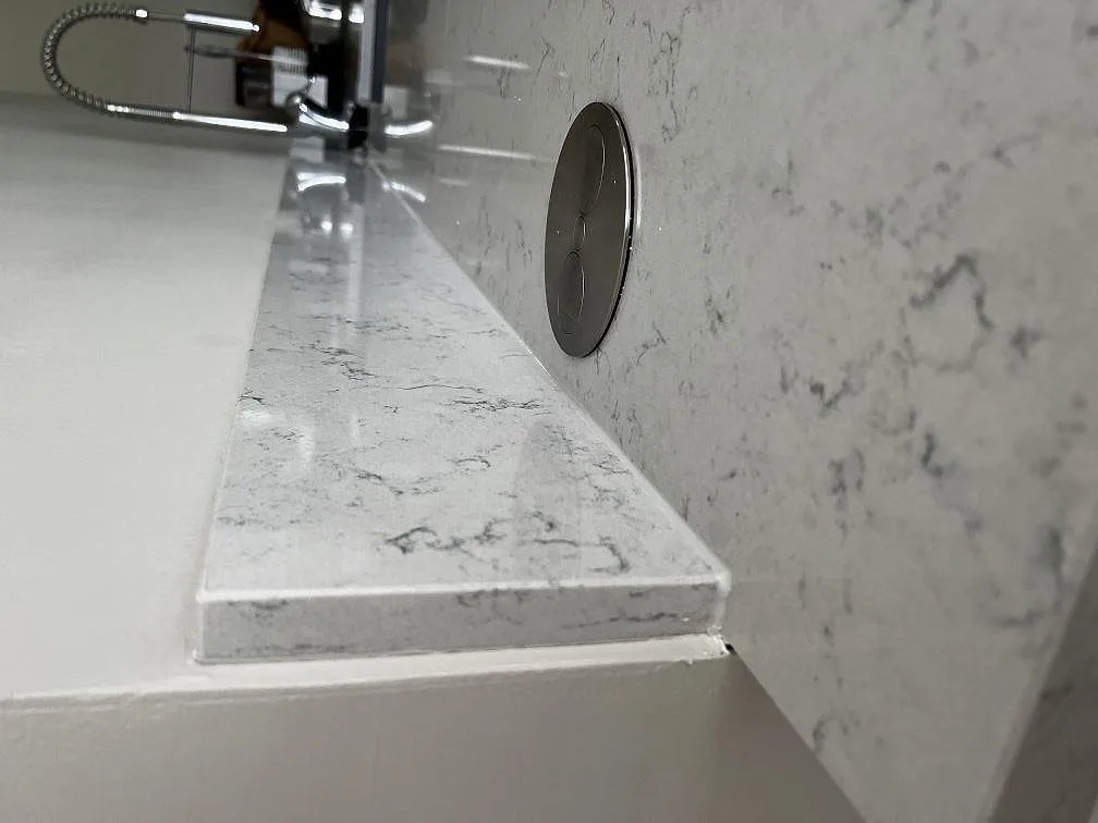 Detalj av polerad kant och eluttag av popup-typ i en bänkskiva av vit Technistone Noble Carrara i ett kök i Kristianstad.