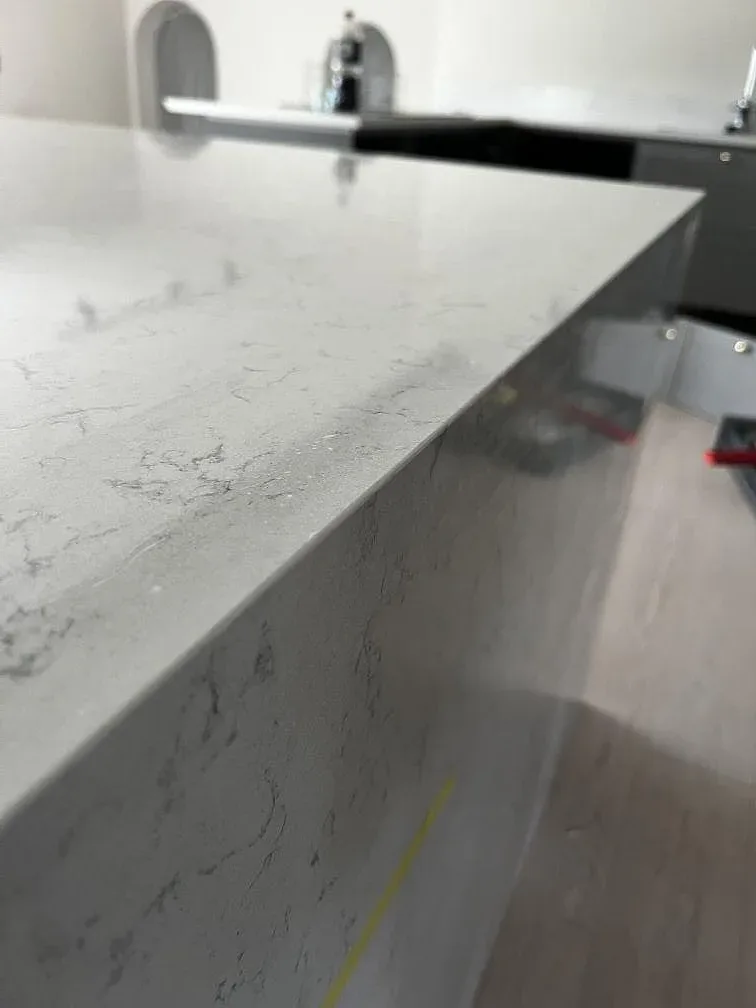 Polerad köksö i vit Technistone Noble Carrara med grå ådring under montering i ett kök i Kristianstad.