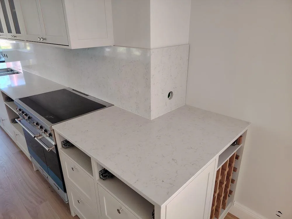 Närbild av polerad Technistone Noble Carrara komposit som bänkskiva och stänkskydd vid spis i kök i Lidingö.