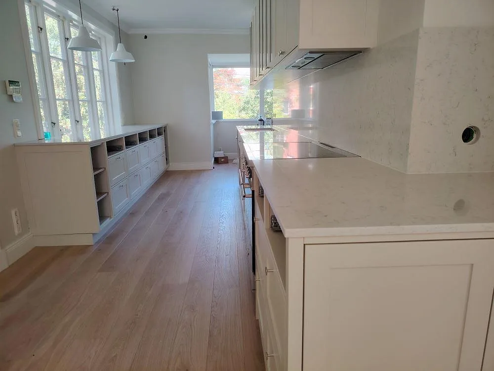 Polerad köksbänkskiva i Technistone Noble Carrara komposit med matchande stänkskydd i ett ljust kök i Lidingö.