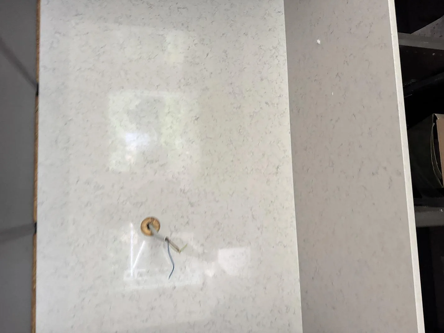 Närbild på polerad Technistone Noble Carrara som stående stendetalj med eluttagshål under köksmontering i Lomma.