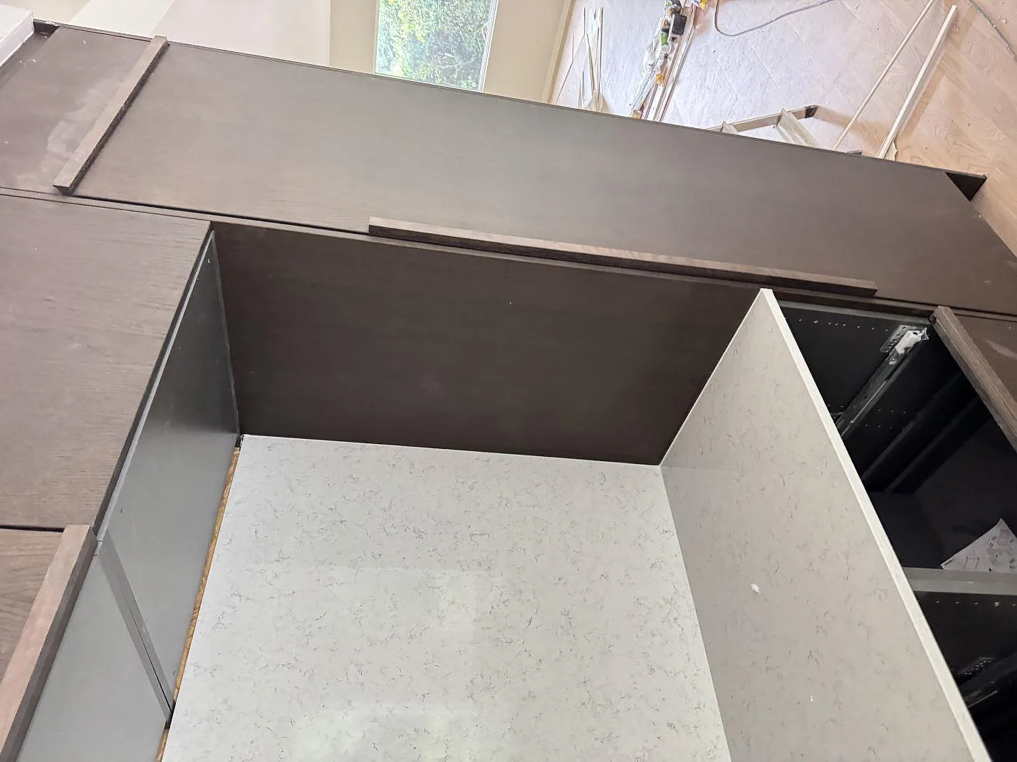Monterad köksbänk och stående skiva i polerad Technistone Noble Carrara komposit intill mörka stommar i Lomma.