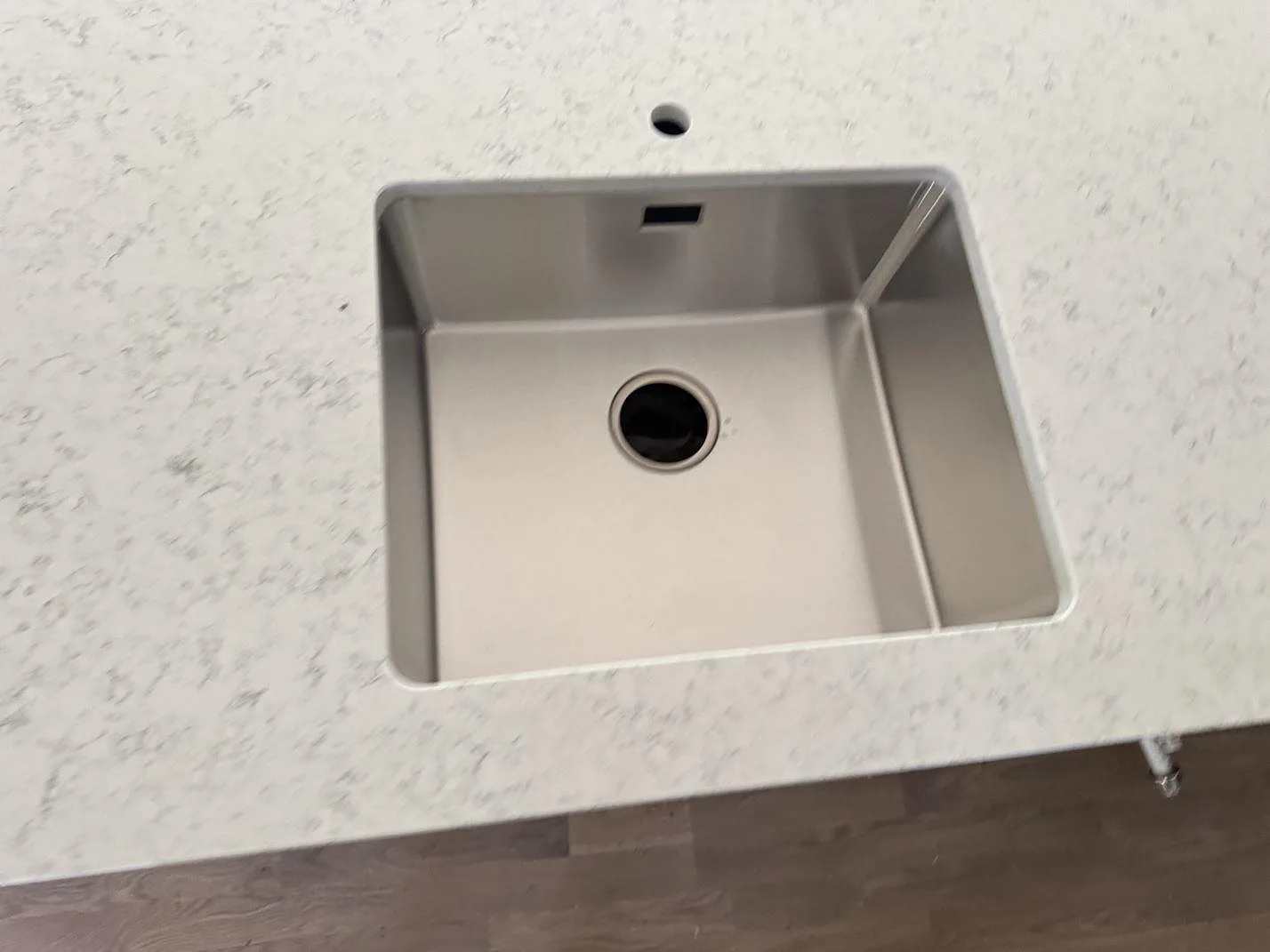 Detalj av underlimmad rostfri diskho i polerad Technistone Noble Carrara komposit med blandarhål i kök i Lomma.