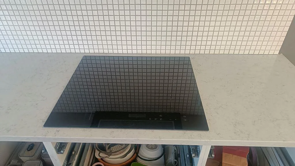 Närbild av polerad Technistone Noble Carrara bänkskiva runt en svart häll i ett kök i Lund.