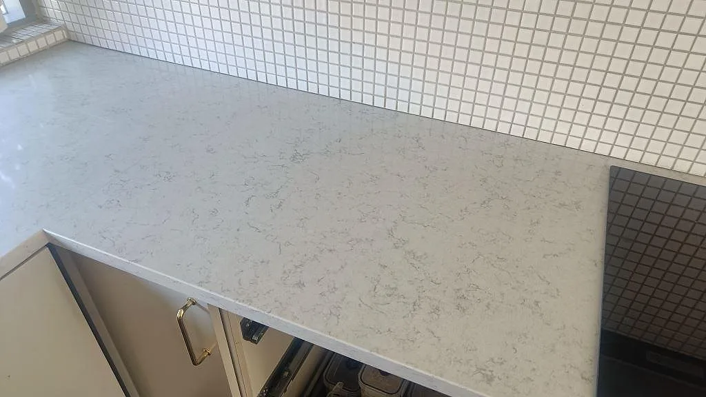 Vit köksbänkskiva i Technistone Noble Carrara, polerad, med grå ådring, mosaik och hällkant i Lund.